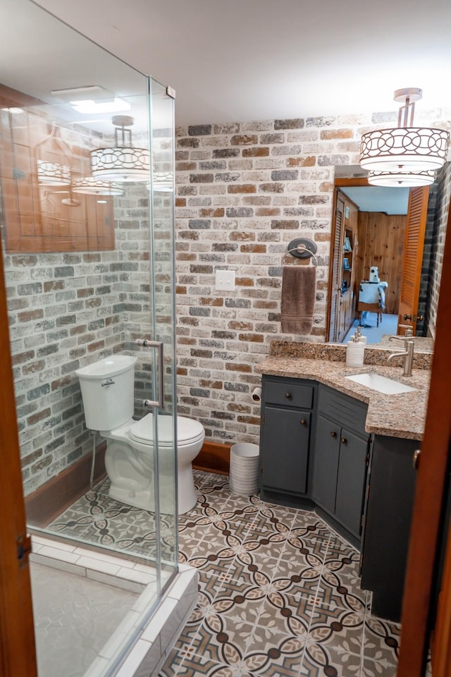 bathroom with tile patterned floors, toilet, brick wall, a shower stall, and vanity