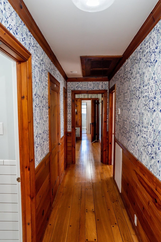 corridor featuring wainscoting, wallpapered walls, crown molding, and hardwood / wood-style flooring