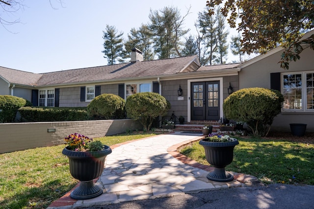 ranch-style home with french doors, a front yard, roof with shingles, and a chimney