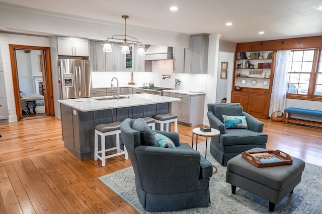 interior space with stainless steel appliances, light wood-style floors, wall chimney range hood, and a sink