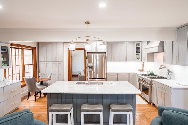 kitchen featuring a breakfast bar, gray cabinets, wall chimney range hood, appliances with stainless steel finishes, and light wood finished floors