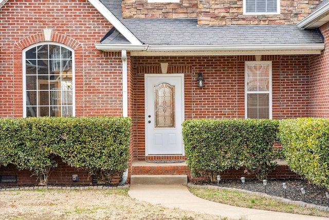 view of exterior entry with brick siding and roof with shingles