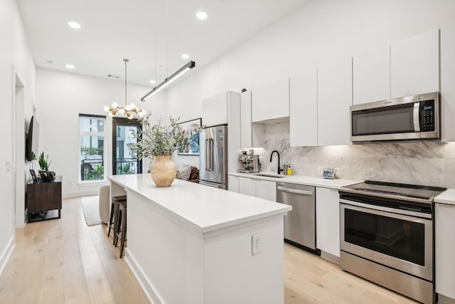 kitchen with a sink, a kitchen island, backsplash, stainless steel appliances, and white cabinets