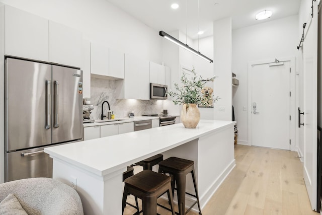 kitchen with a kitchen bar, decorative backsplash, appliances with stainless steel finishes, white cabinets, and a sink