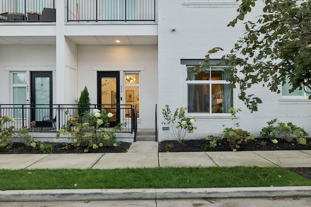 doorway to property with a porch, a balcony, and brick siding