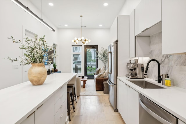 kitchen with a sink, tasteful backsplash, appliances with stainless steel finishes, white cabinets, and light countertops