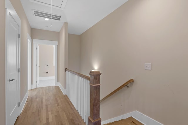 hallway with visible vents, baseboards, attic access, light wood-style floors, and an upstairs landing