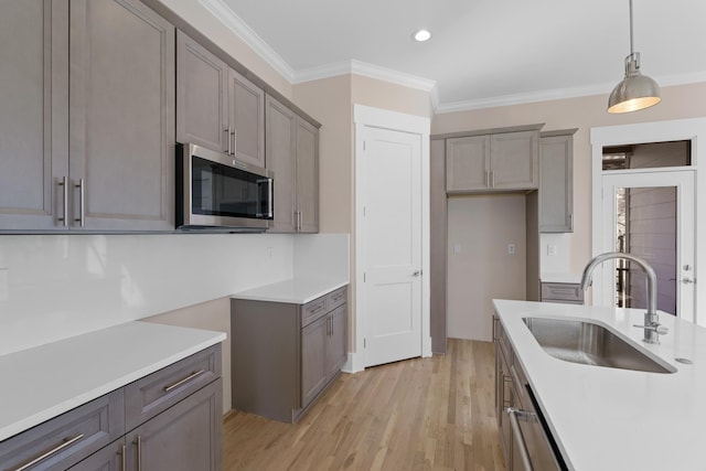 kitchen featuring gray cabinetry, a sink, light countertops, crown molding, and stainless steel microwave