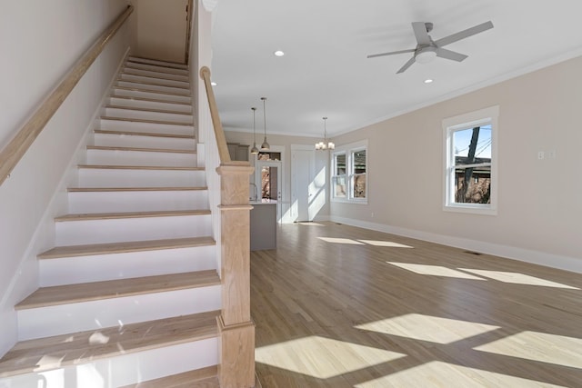 stairs with ornamental molding, ceiling fan with notable chandelier, wood finished floors, recessed lighting, and baseboards