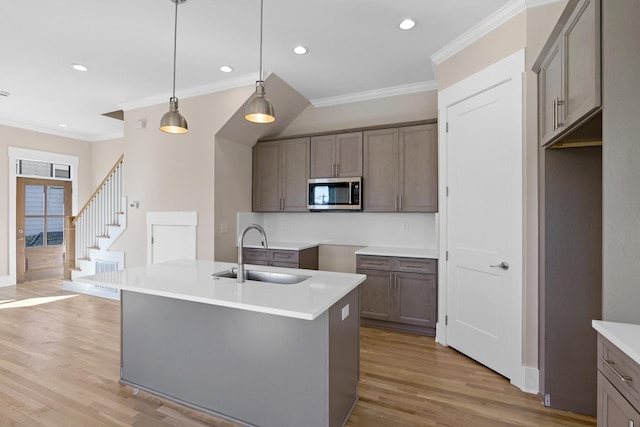 kitchen with stainless steel microwave, pendant lighting, light wood-type flooring, ornamental molding, and a sink