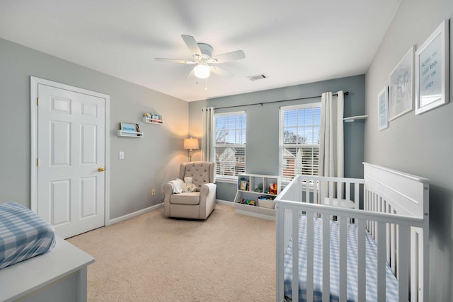 bedroom with visible vents, a crib, ceiling fan, baseboards, and carpet floors