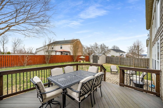 wooden deck with a storage unit, a lawn, a fenced backyard, an outdoor structure, and outdoor dining area