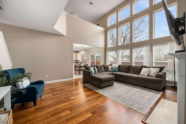 living area with an inviting chandelier, a high ceiling, baseboards, and hardwood / wood-style floors