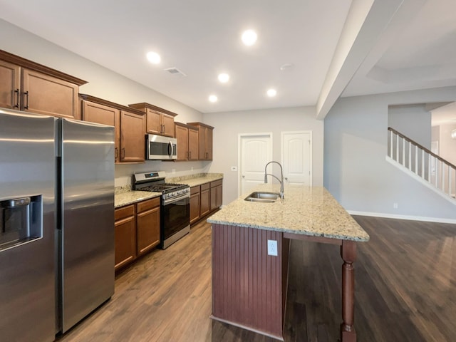 kitchen featuring dark wood finished floors, an island with sink, light stone counters, appliances with stainless steel finishes, and a sink