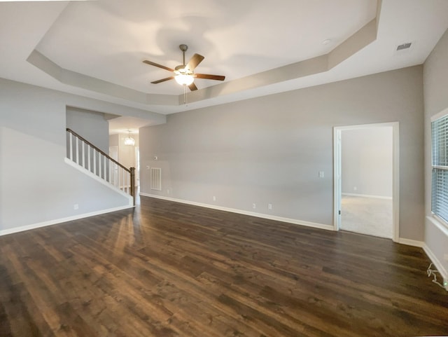 unfurnished living room featuring baseboards, dark wood-type flooring, and a tray ceiling