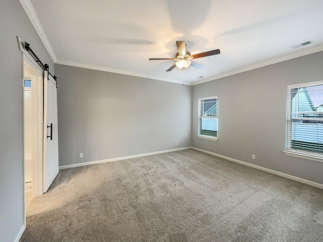 carpeted spare room featuring a ceiling fan, visible vents, baseboards, ornamental molding, and a barn door