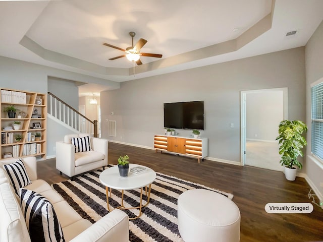 living room with a raised ceiling, wood finished floors, baseboards, and visible vents