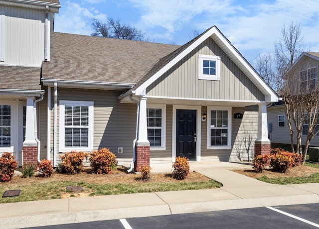 view of front of property featuring brick siding, a shingled roof, central AC, and uncovered parking