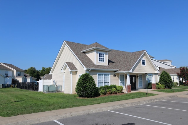 view of front of property featuring a front yard, fence, roof with shingles, and uncovered parking