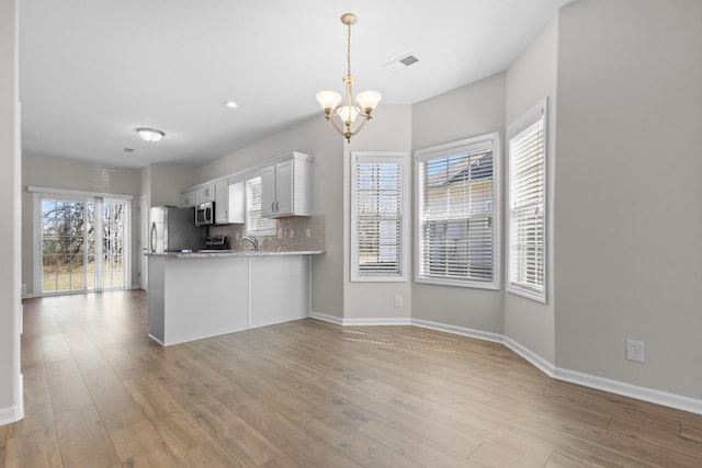 kitchen featuring decorative backsplash, stainless steel microwave, light wood finished floors, and a chandelier