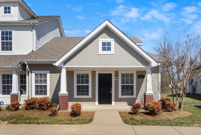 view of front of house with covered porch, brick siding, and roof with shingles