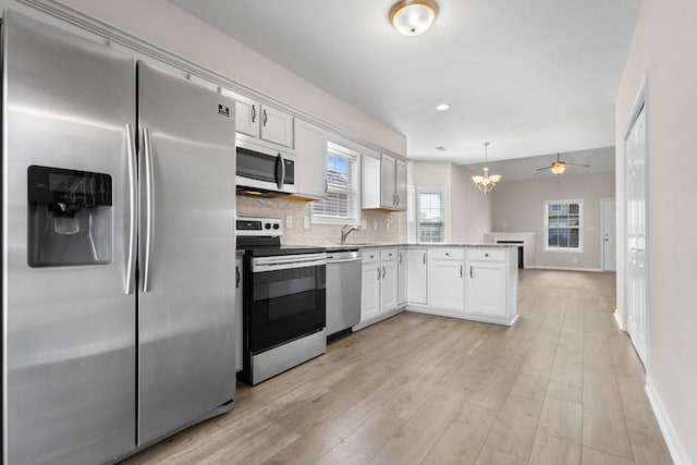 kitchen featuring tasteful backsplash, white cabinetry, stainless steel appliances, light wood-style floors, and a peninsula