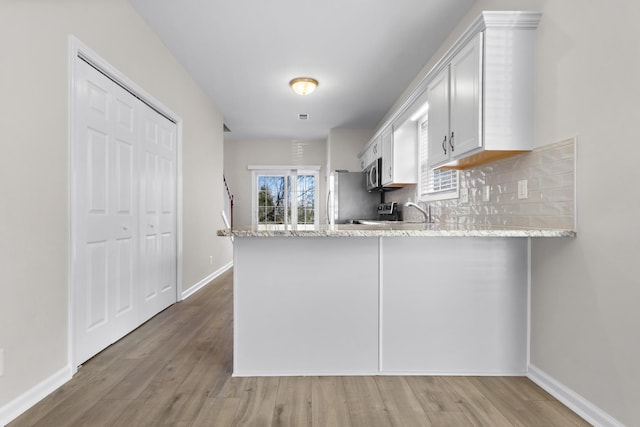 kitchen with light stone countertops, decorative backsplash, a peninsula, wood finished floors, and stainless steel appliances