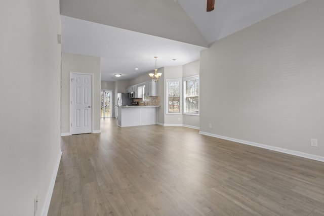 unfurnished living room featuring lofted ceiling, a healthy amount of sunlight, wood finished floors, and ceiling fan with notable chandelier