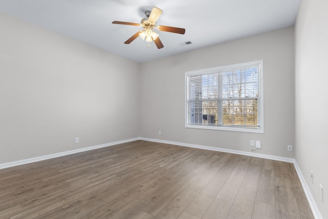 spare room with a ceiling fan, wood finished floors, visible vents, and baseboards