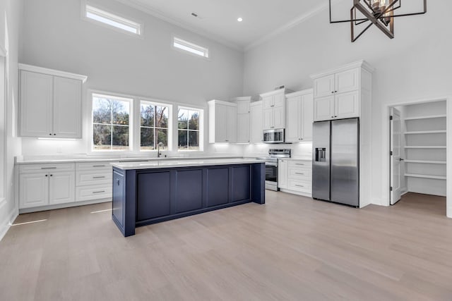 kitchen with light countertops, a towering ceiling, appliances with stainless steel finishes, crown molding, and a center island