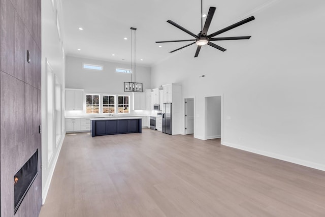 unfurnished living room featuring ceiling fan with notable chandelier, recessed lighting, a high ceiling, light wood finished floors, and baseboards