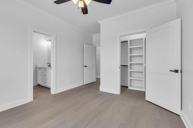 unfurnished bedroom featuring a walk in closet, crown molding, light wood-style flooring, and baseboards