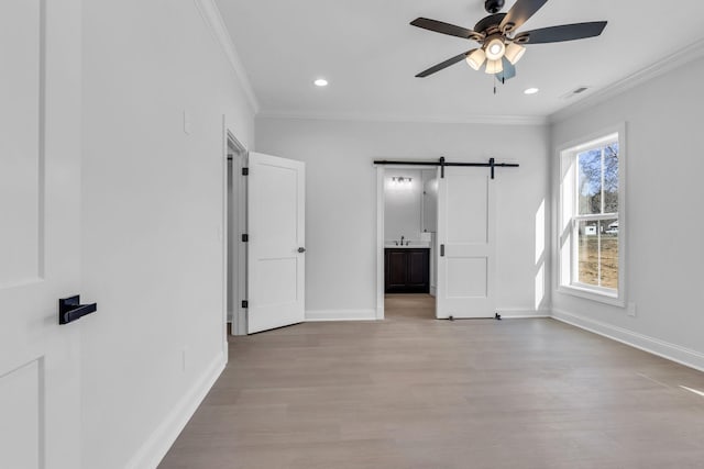 unfurnished bedroom with a barn door, wood finished floors, crown molding, and baseboards