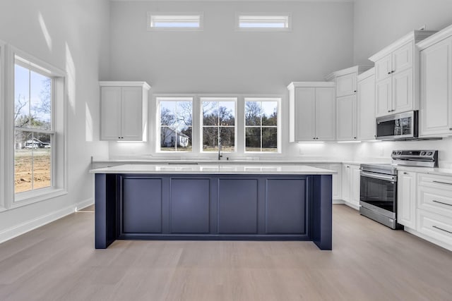 kitchen featuring white cabinetry, a towering ceiling, appliances with stainless steel finishes, and a kitchen island