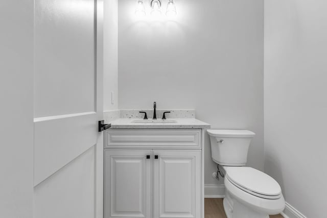 half bath featuring toilet, vanity, baseboards, and wood finished floors