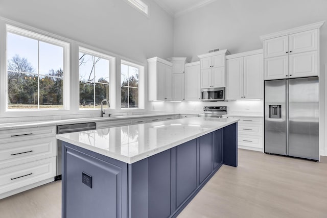 kitchen featuring light stone counters, white cabinets, a center island, and stainless steel appliances