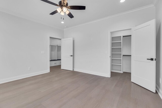 unfurnished bedroom featuring wood finished floors, a walk in closet, baseboards, and ornamental molding