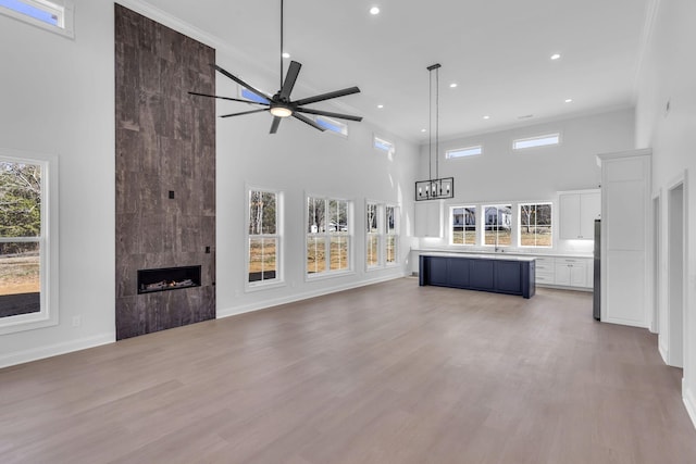 unfurnished living room featuring light wood-style flooring, a healthy amount of sunlight, baseboards, and a tile fireplace