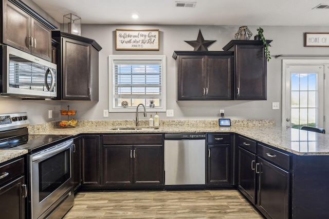 kitchen featuring visible vents, a peninsula, light wood-style floors, stainless steel appliances, and a sink