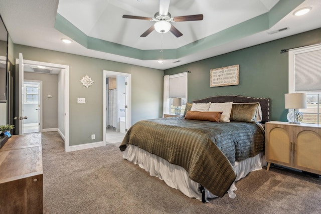 carpeted bedroom with a ceiling fan, baseboards, visible vents, ensuite bathroom, and a raised ceiling