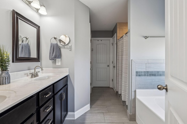 full bathroom with double vanity, a tub to relax in, baseboards, and a sink