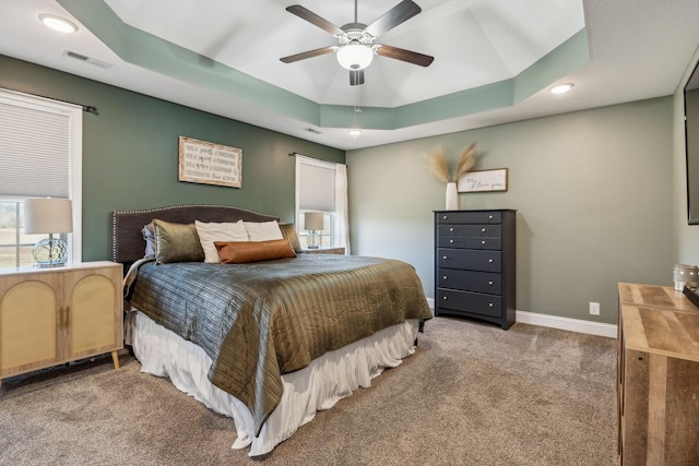 carpeted bedroom featuring a raised ceiling, multiple windows, baseboards, and visible vents