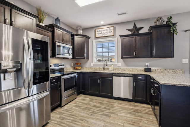 kitchen with visible vents, light wood-style flooring, a sink, light stone counters, and appliances with stainless steel finishes