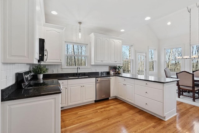 kitchen featuring a peninsula, a sink, stainless steel appliances, vaulted ceiling, and dark countertops