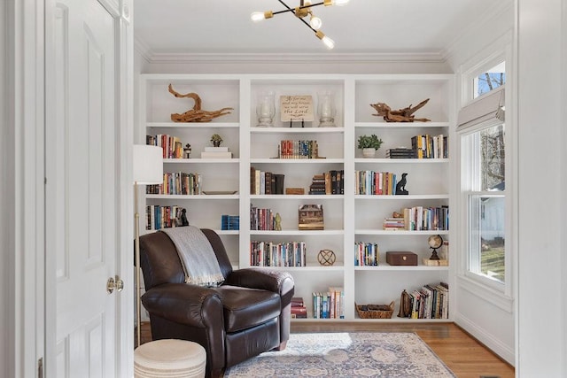 sitting room with built in features, crown molding, an inviting chandelier, and wood finished floors