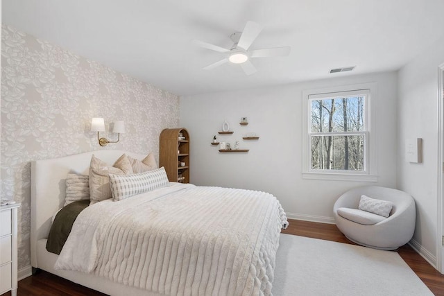 bedroom featuring dark wood-style floors, visible vents, wallpapered walls, and baseboards