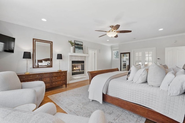 bedroom with wood finished floors, recessed lighting, ornamental molding, french doors, and a glass covered fireplace