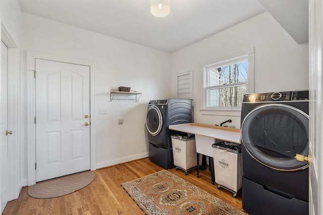 clothes washing area featuring laundry area, separate washer and dryer, light wood-type flooring, and baseboards