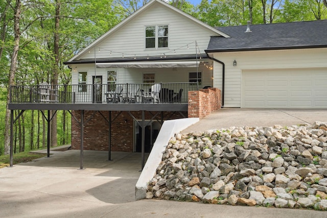 view of front of house with driveway, a deck, a shingled roof, an attached garage, and brick siding