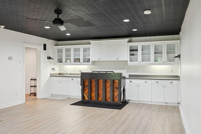 kitchen with white cabinets, light wood finished floors, a ceiling fan, a sink, and baseboards